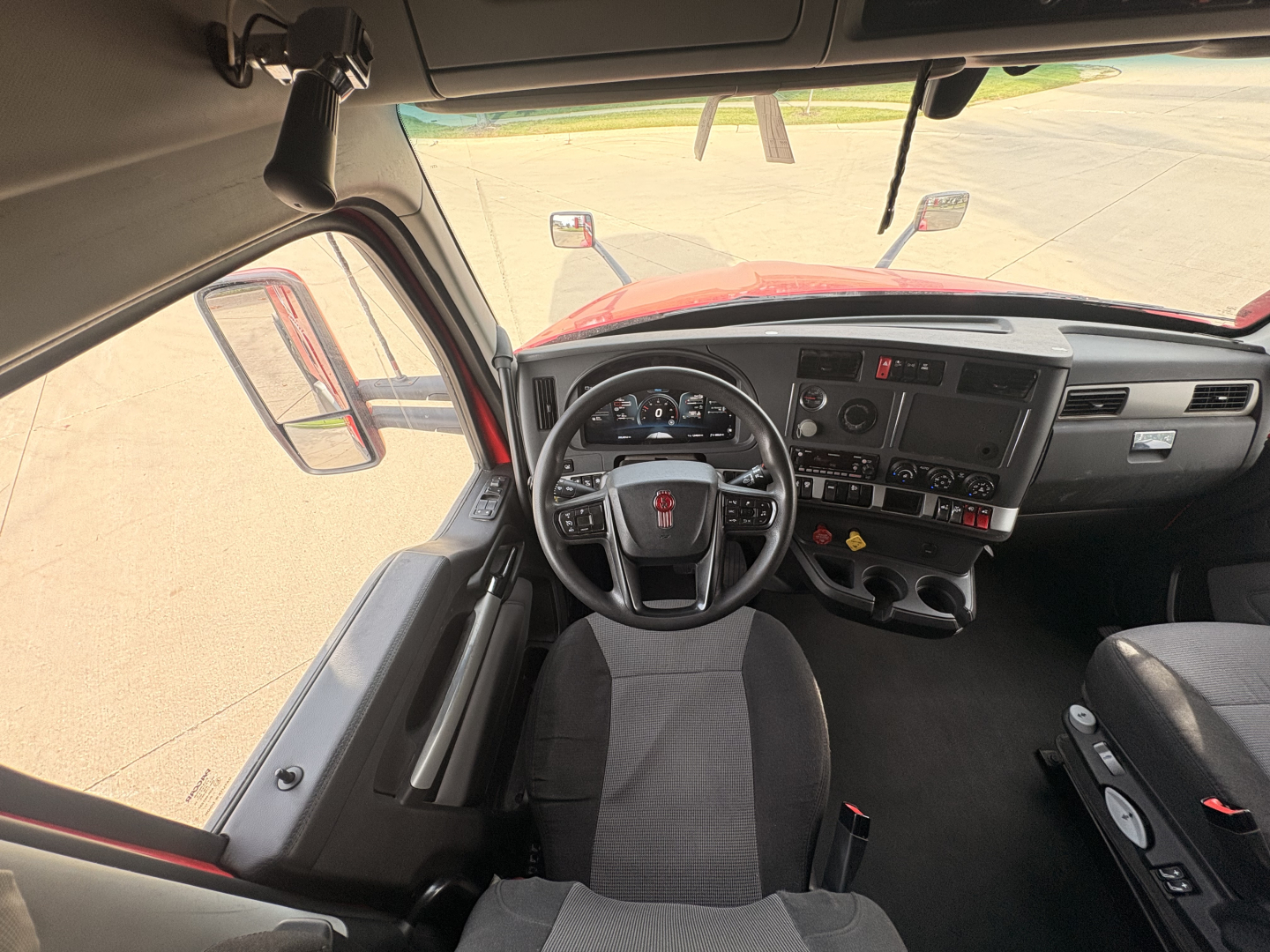 Kenworth T680 truck cabin interior showing steering wheel, dashboard, and driver's seat with side window and mirrors visible.