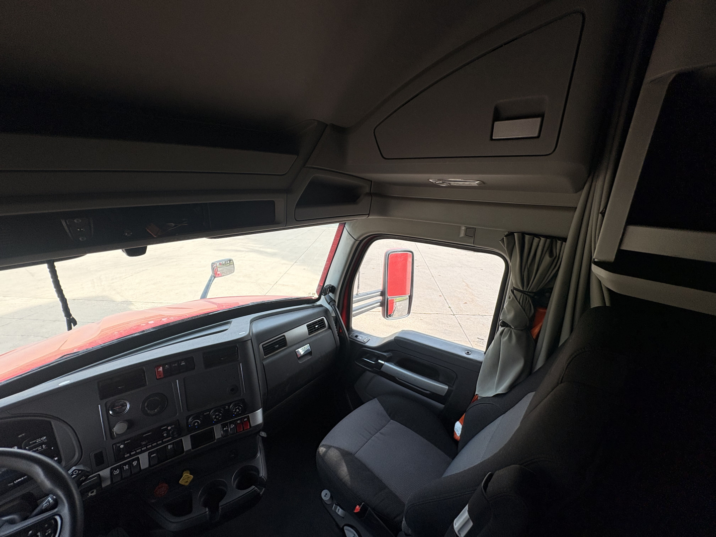 Kenworth T680 truck cabin interior viewing driver seat and dashboard with steering wheel and visibility of side mirror.