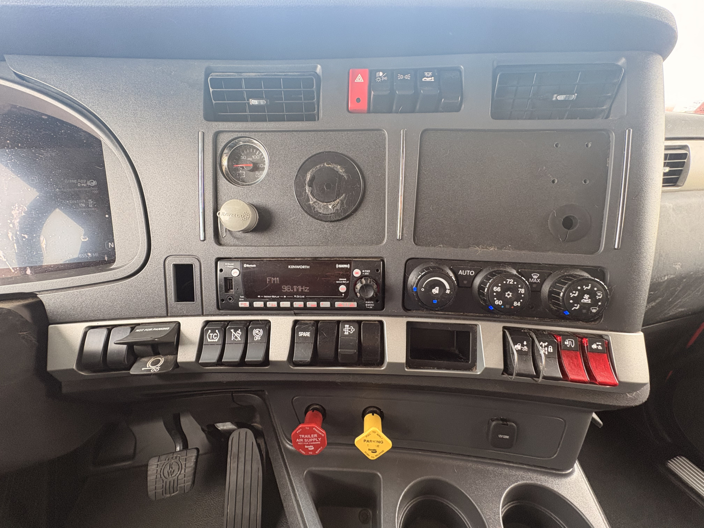 Kenworth T680 dashboard panel showing gauges, climate controls, and storage compartments; ignition area with red and yellow key tags; center console switches visible.