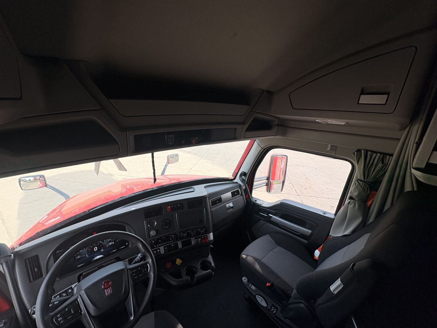 Kenworth T680 interior cab view from driver side showing dashboard, steering wheel, and passenger seat.