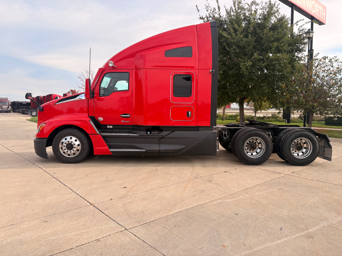 Kenworth T680 tractor in red, side view showing sleeper cab, long wheelbase, dual rear axles, and fuel tanks.