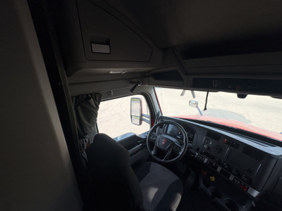 Truck cab interior of a Kenworth T680 2023 showing steering wheel and dashboard from passenger side with center console and driver seat.