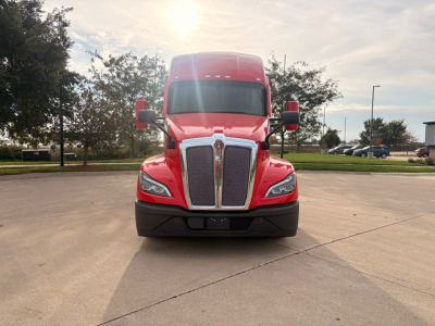 Kenworth T680 front view showing bold grille, headlights, and red cab in a parking lot.