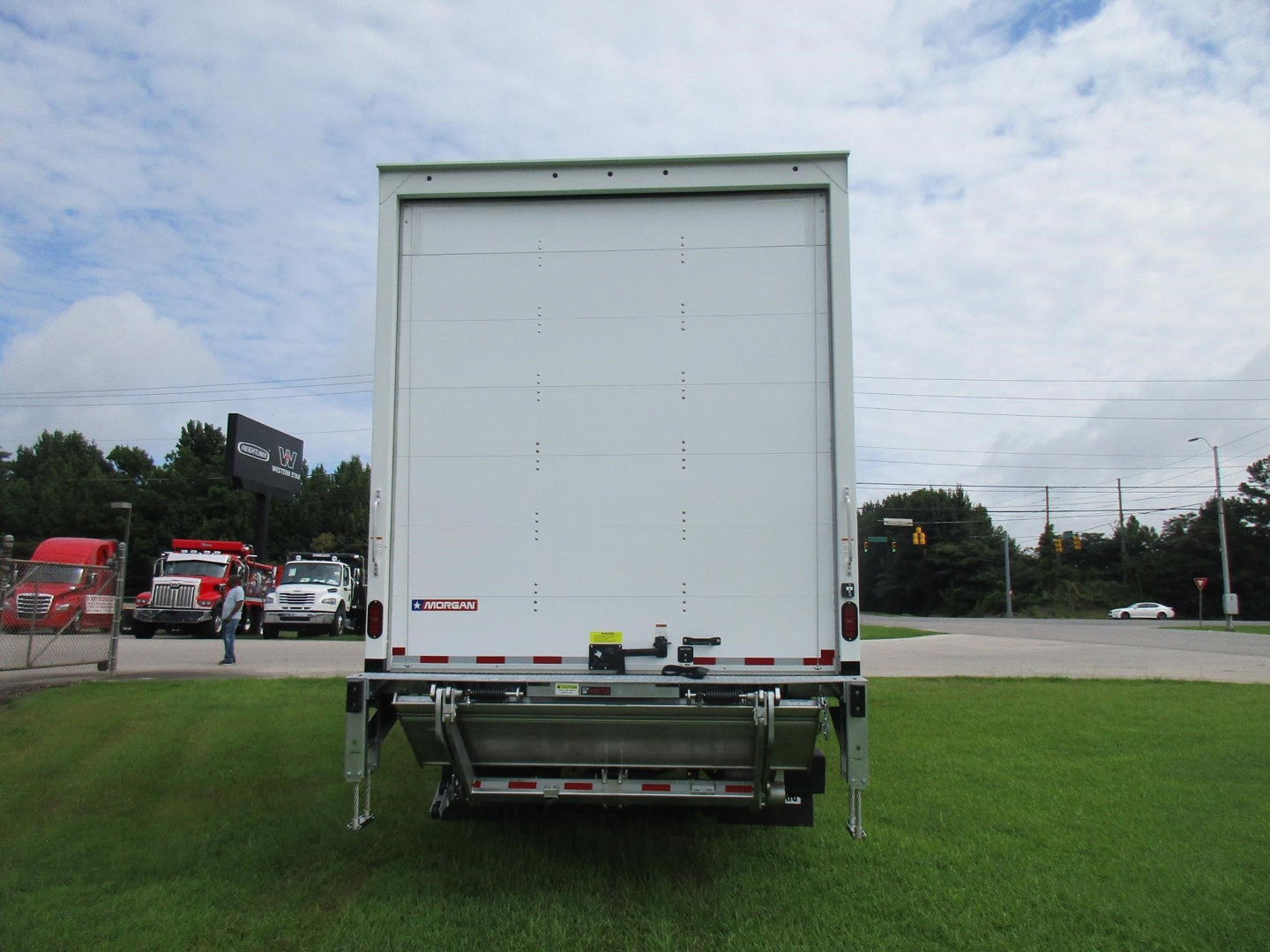 Rear view of a new Freightliner M2 106 box truck with liftgate, white cargo area, and chrome bumper.