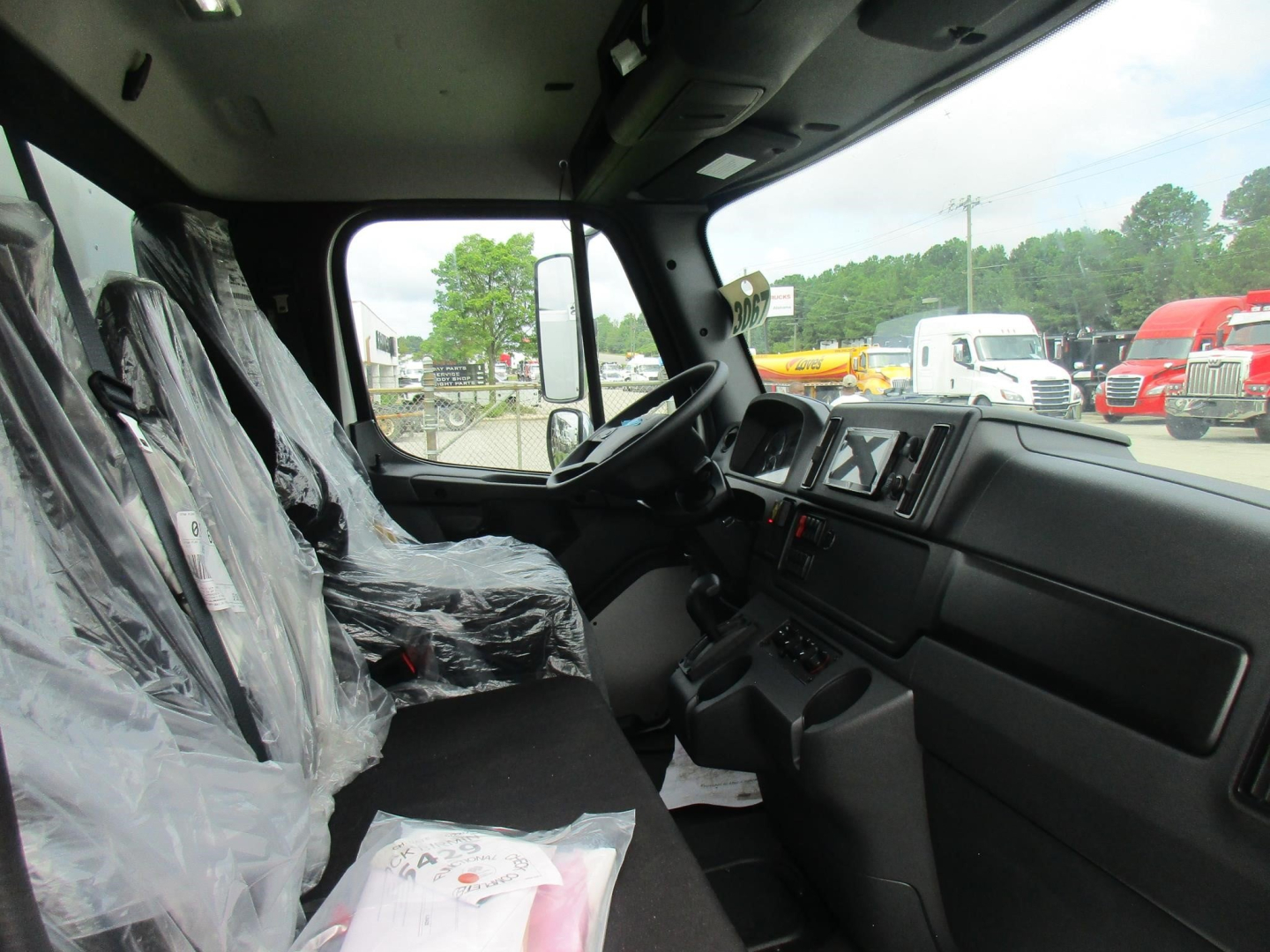 Cab interior of a new Freightliner M2 106 truck showing front seats and dashboard with protective plastic on seats.