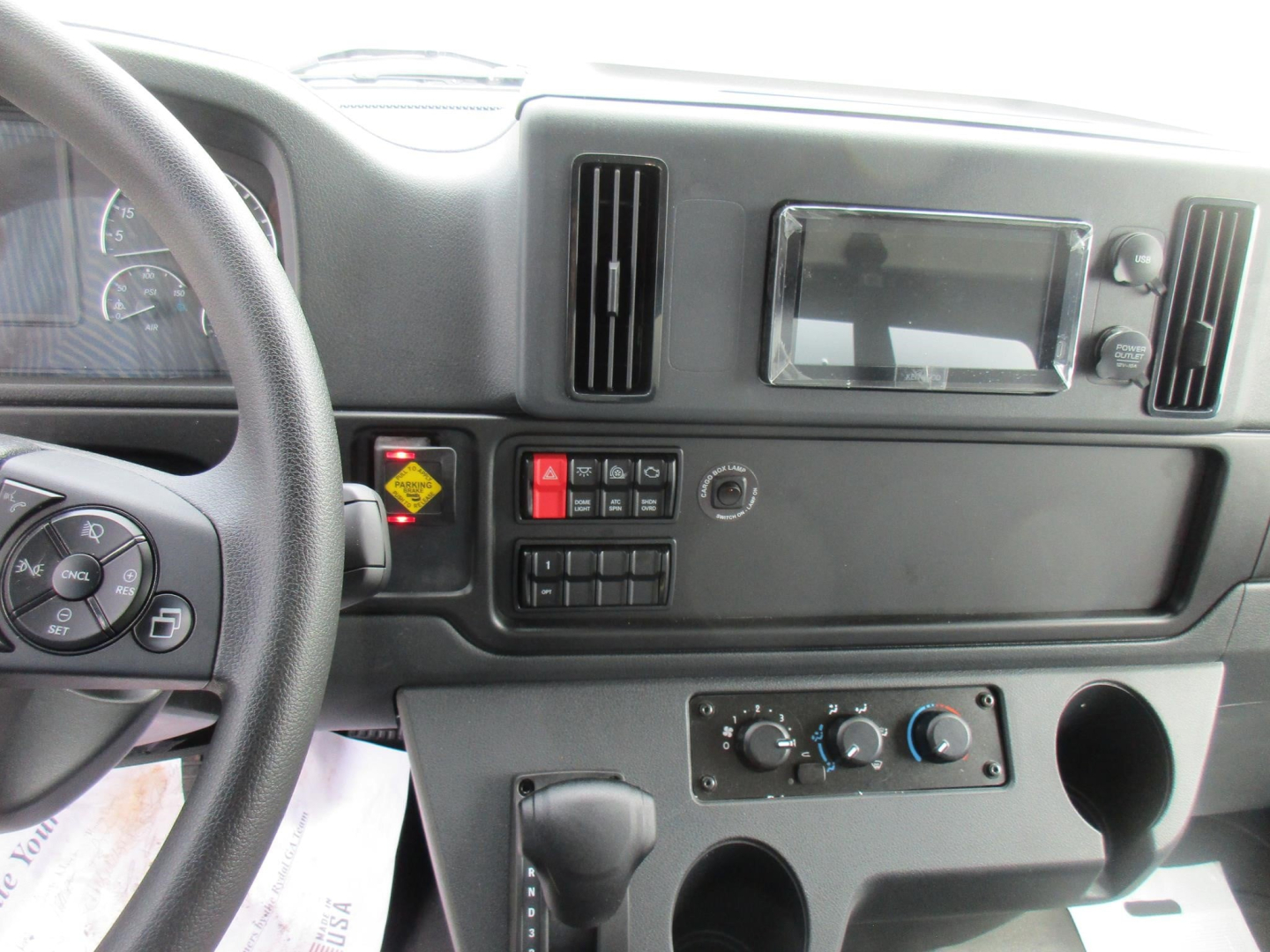 Dashboard cabin of a Freightliner M2 106 showing steering wheel, center console with controls, infotainment screen, air vents, and climate control knobs.