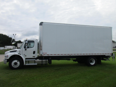 Freightliner M2 106 box truck side view with white cab and large rectangular cargo box on a grassy lot.
