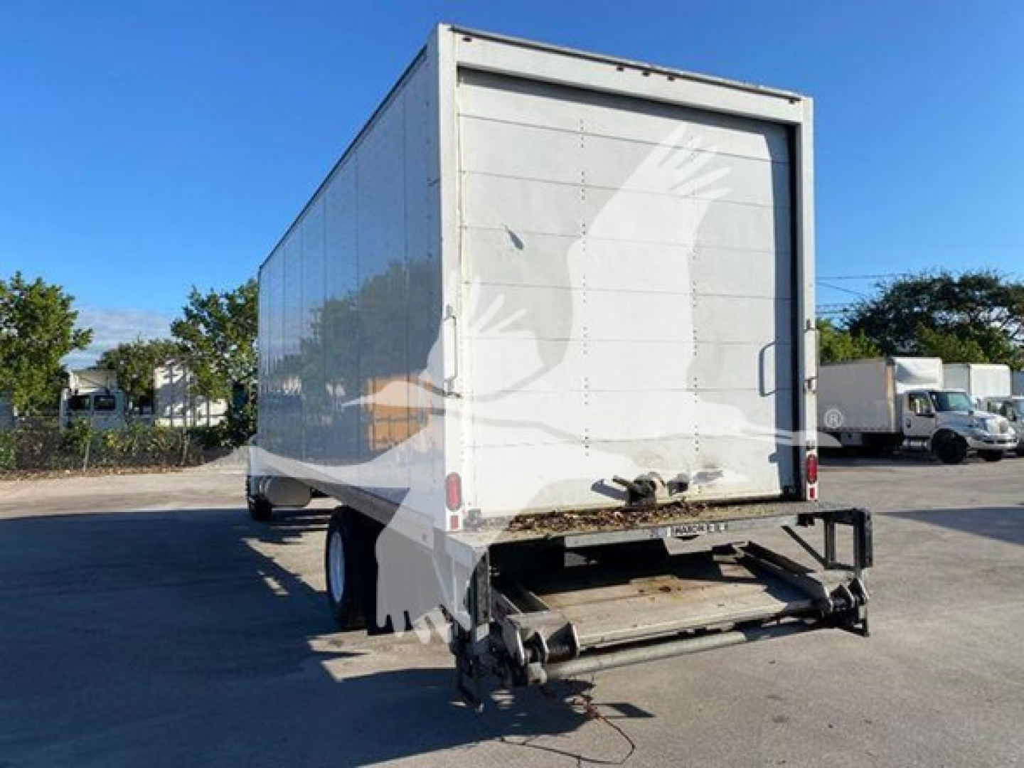 Box truck rear showing roll-up door and trailer hitch under clear sky.