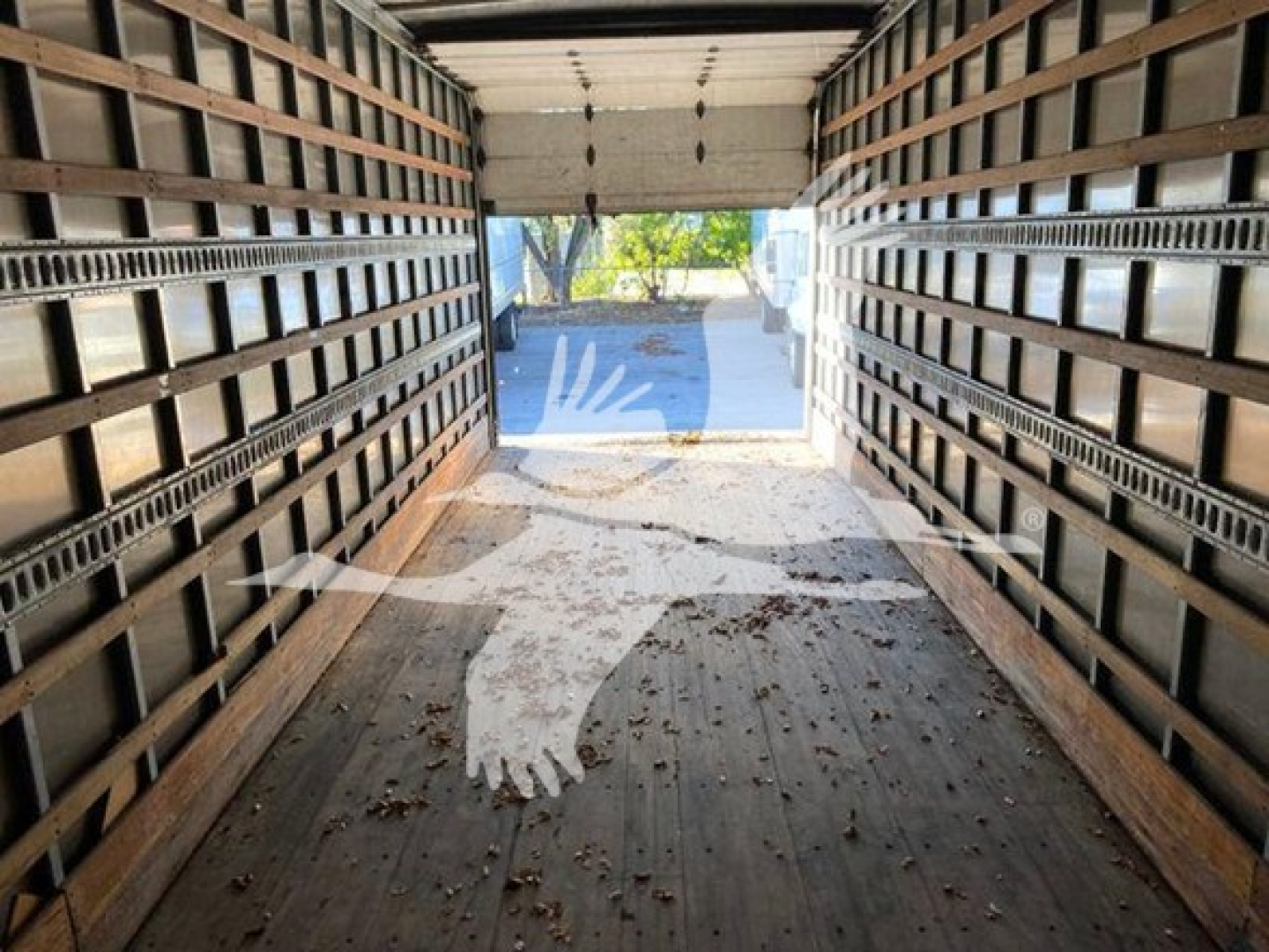 Interior of a boxed cargo truck with wooden side rails and open rear doors; view toward outdoors with tree and driveway visible.