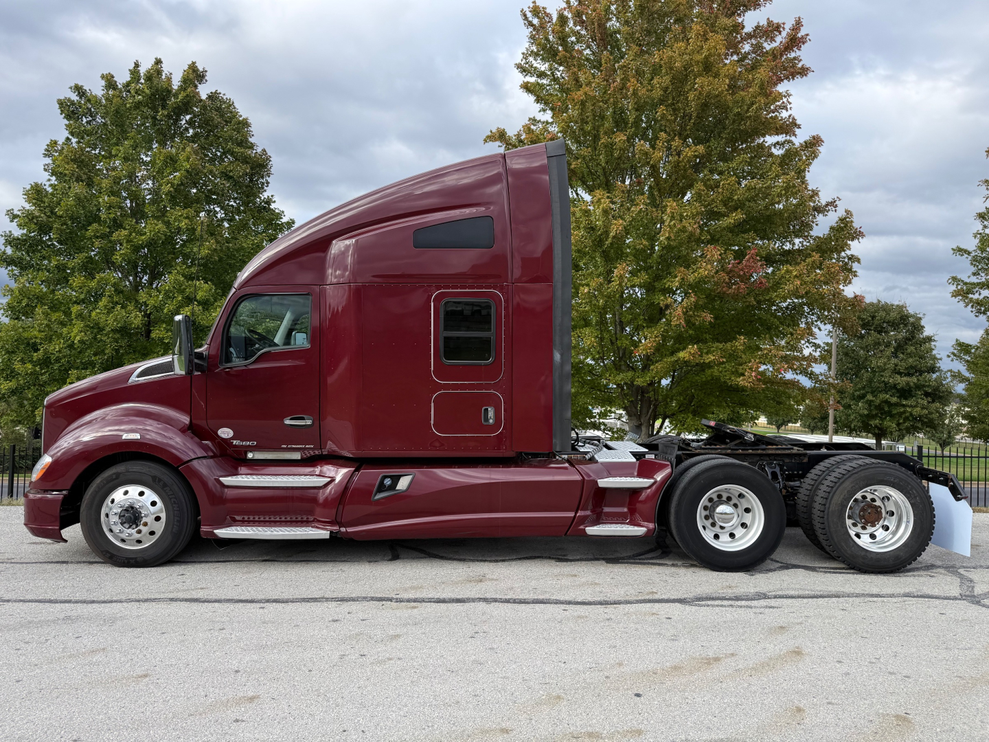 Kenworth T680 conventional sleeper tractor in maroon showing cab side profile and rear wheels.