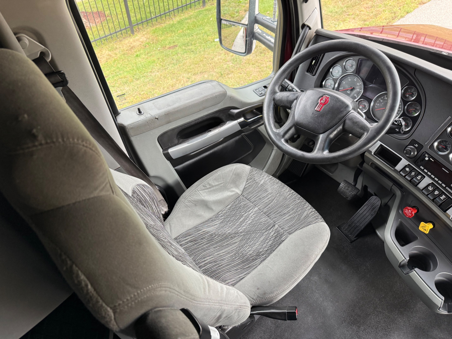 Kenworth T680 interior showing steering wheel and dashboard with gray cloth seat and controls.