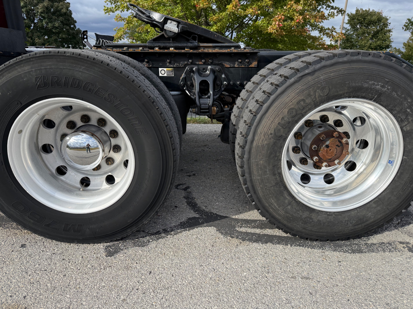 Kenworth T680 axle area showing two rear wheels, dual chrome rims, visible tire treads, and chassis undercarriage.