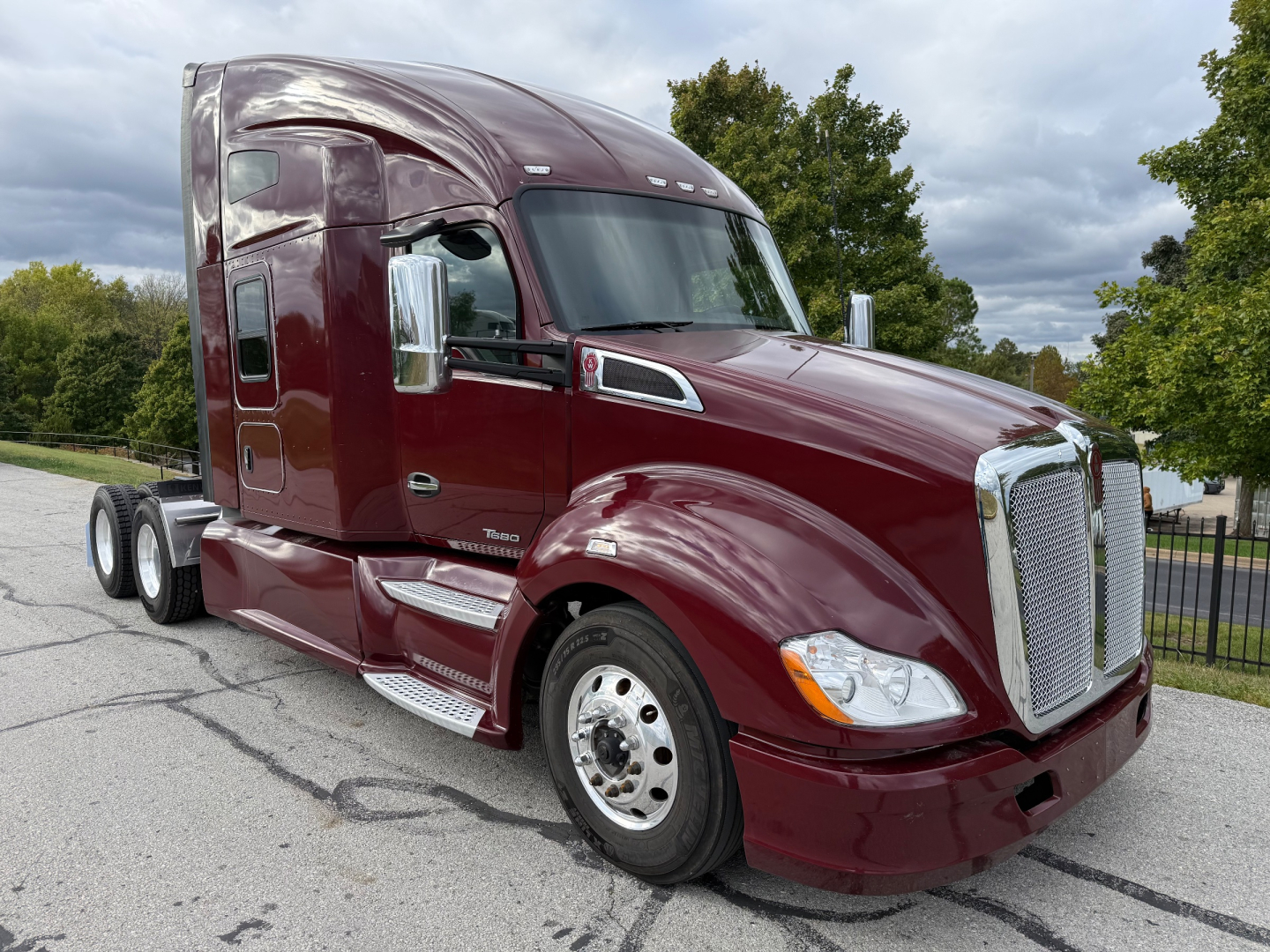 Kenworth T680 tractor in burgundy showing chrome grille and dual rear wheels, cab with sleeper, highway setting.