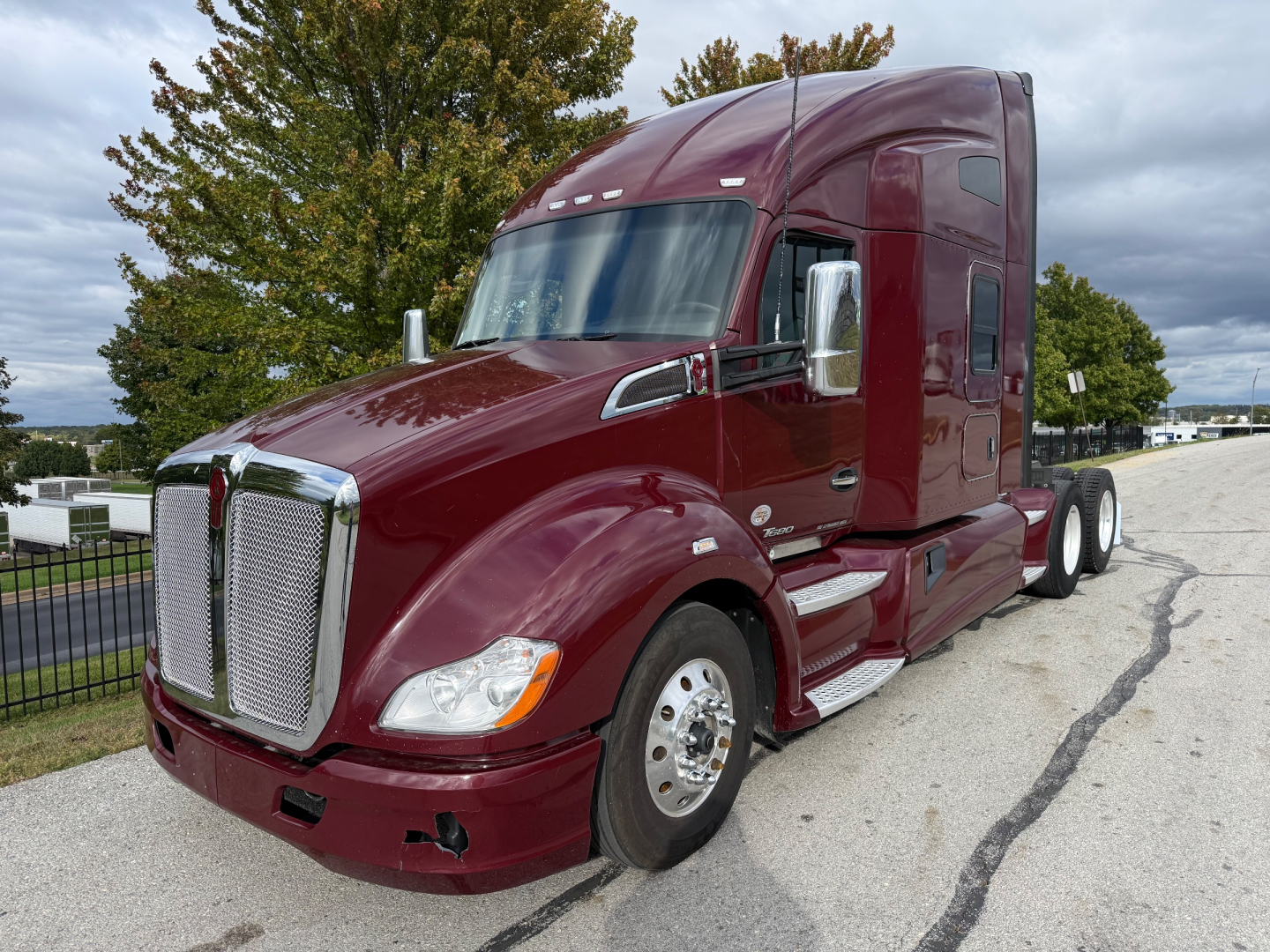 Kenworth T680 tractor in maroon showing aerodynamic hood and chrome grille with sleeper cab. VIN plate not visible; side mirrors and wheels visible.