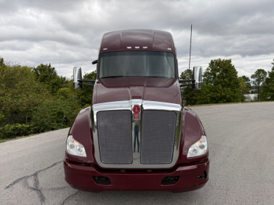 Kenworth truck front view showing large chrome grille, maroon body, dual headlights, and side mirrors.