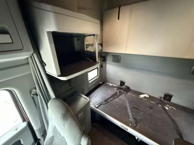 Kenworth T680 sleeper cab interior showing bunk with strap and overhead shelf area, cargo area, and window; view from cabin corner.