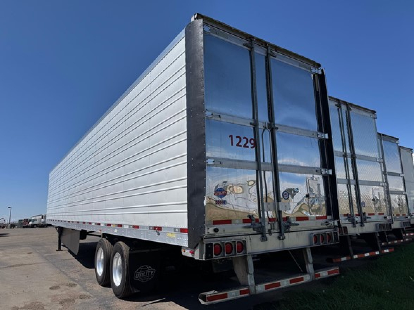 Utility trailer showing outer side and rear doors with stacked wheels and reflective tape.