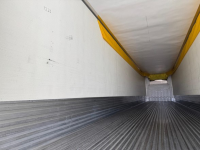 Trailer interior showing empty cargo area with metal ribbed floor, white side walls, and yellow tarpaulin rail covers.