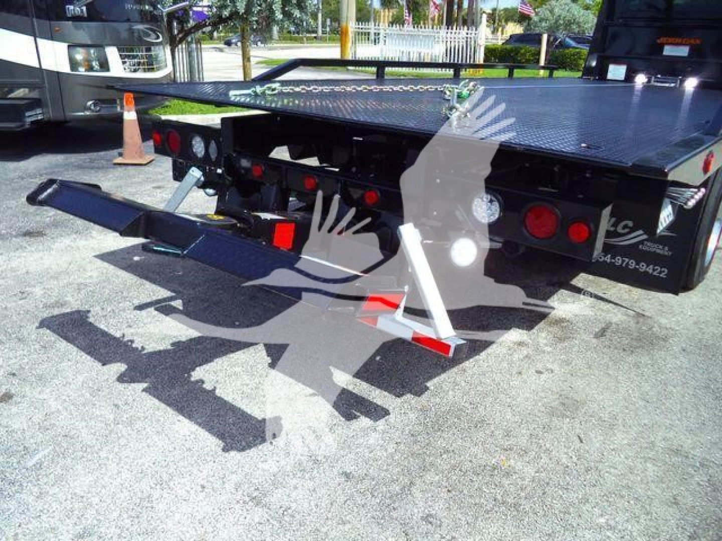 Back view of a 2027 International MV rollback truck bed showing the hydraulic lift and rear platform with safety cones and lights.