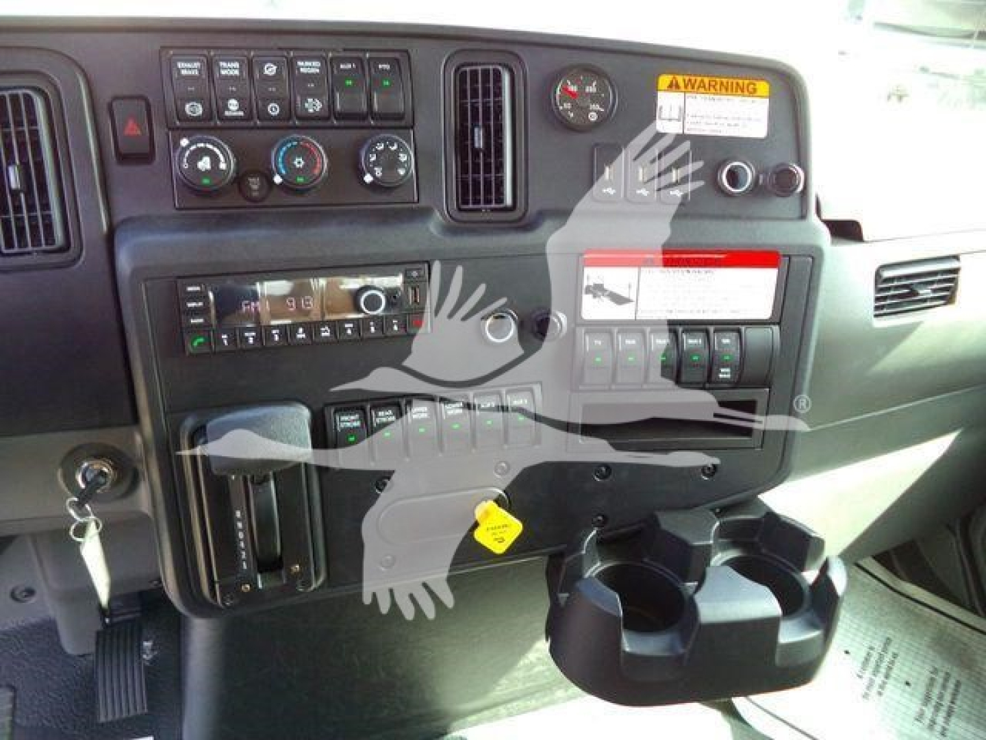Dashboard view of a 2027 International MV showing control gauges, vents, warning sticker, cup holder, and various switches.