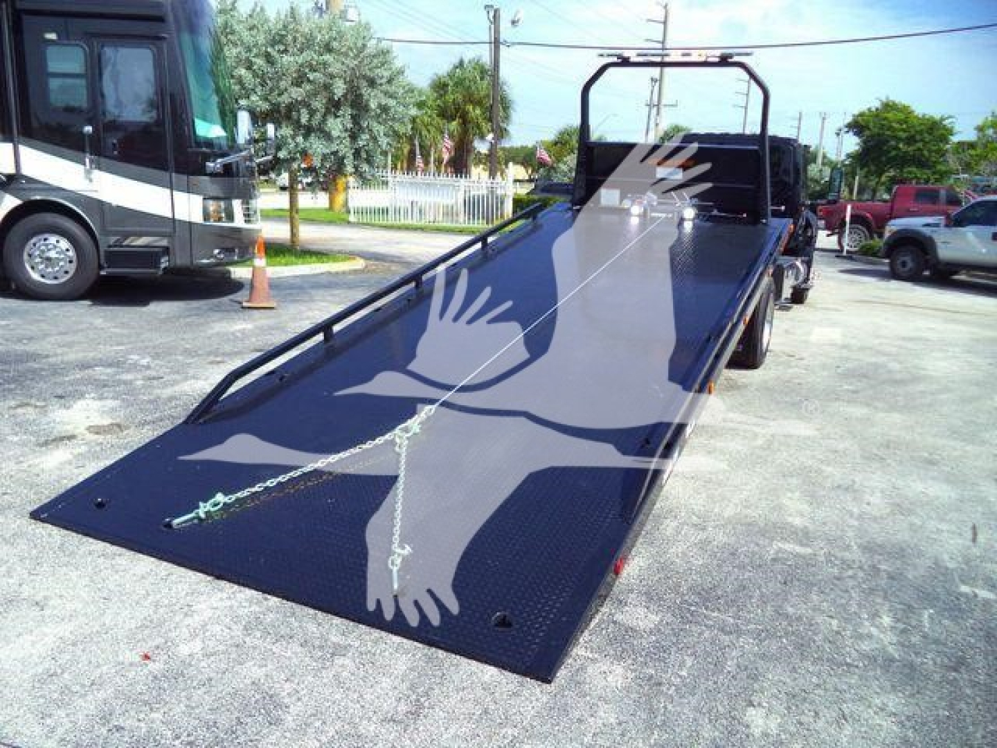 Flatbed tow truck ramp with black diamond plate surface and side rails, extended from rear of a rollback truck, parked in lot