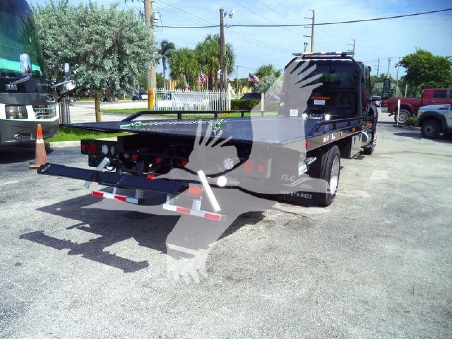 Tow truck flatbed rollback in an open lot showing rear view with extendable ramp and backup lighting.