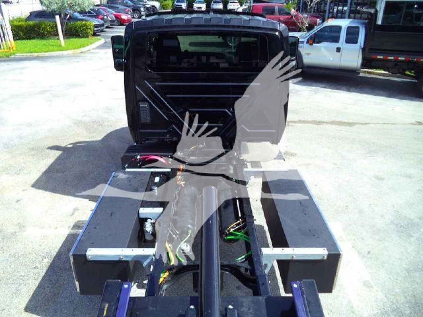 Flatbed truck chassis with dual tool boxes and exposed hydraulic hoses, MV607EXCABBLK sticker area visible in background.