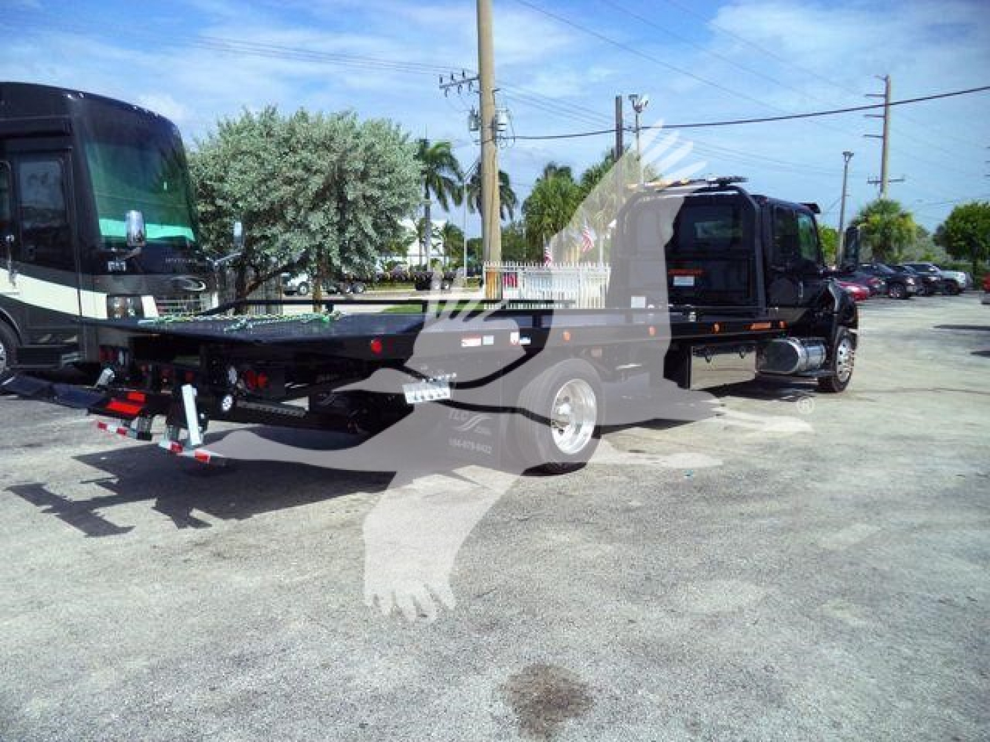 Truck chassis and rollback equipment showing rear view with black cab and towing platform under bright outdoor light.