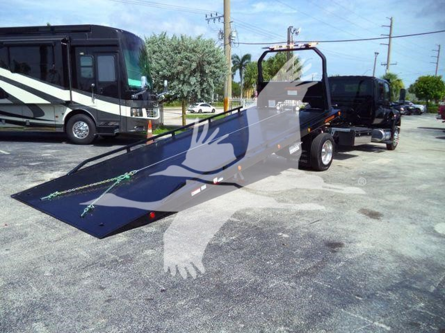 Truck bed with a ramp attached, side view of a rollback tow truck with black chassis and a black flatbed in a parking lot.