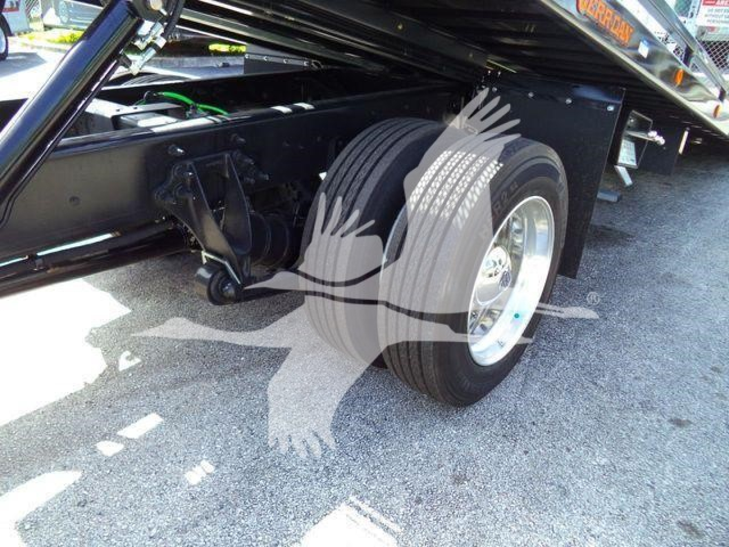 Truck chassis with dual rear wheels and rollback equipment visible; hydraulic hook linkage and flatbed undercarriage; wheel and tire prominent.