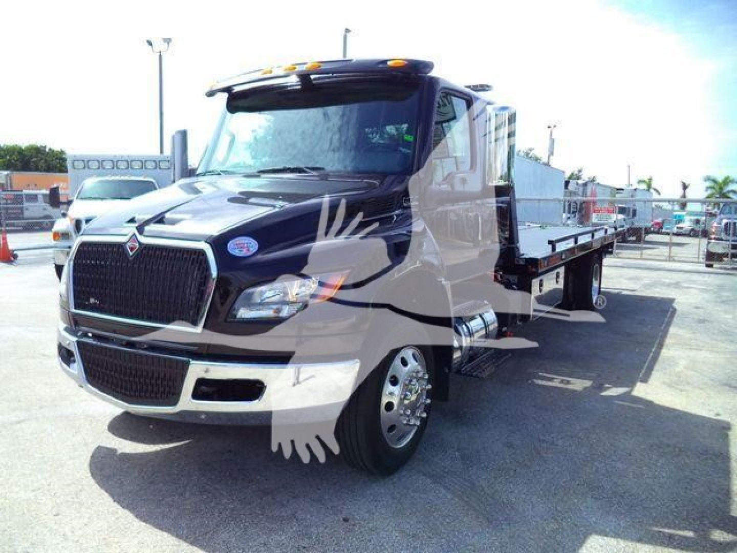 Truck cab and flatbed tow truck by International MV, front-left view, black and white paint with logo, stock image shows rollback equipment