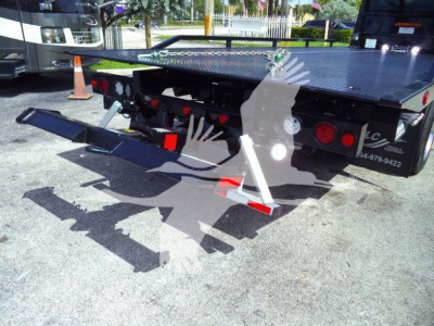 Back view of a 2027 International MV rollback truck bed showing the hydraulic lift and rear platform with safety cones and lights.