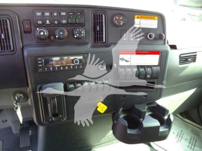 Dashboard view of a 2027 International MV showing control gauges, vents, warning sticker, cup holder, and various switches.