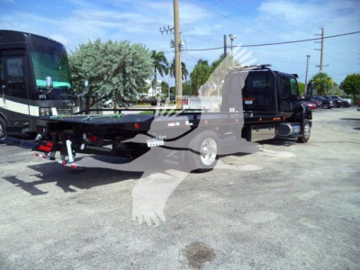Truck chassis and rollback equipment showing rear view with black cab and towing platform under bright outdoor light.
