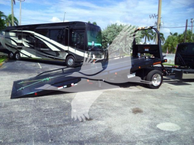 Motorhome with a tow dolly/flatbed trailer in the foreground and a large black and whiteCelebrity style motorhome in the background.