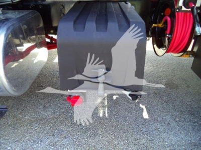 Tractor-trailer rear view showing black fuel/auxiliary tank with red tow eye and hooks, hoses coiled on right, and reflection of birds; MV607EXCABBLK stock number tag not visible.