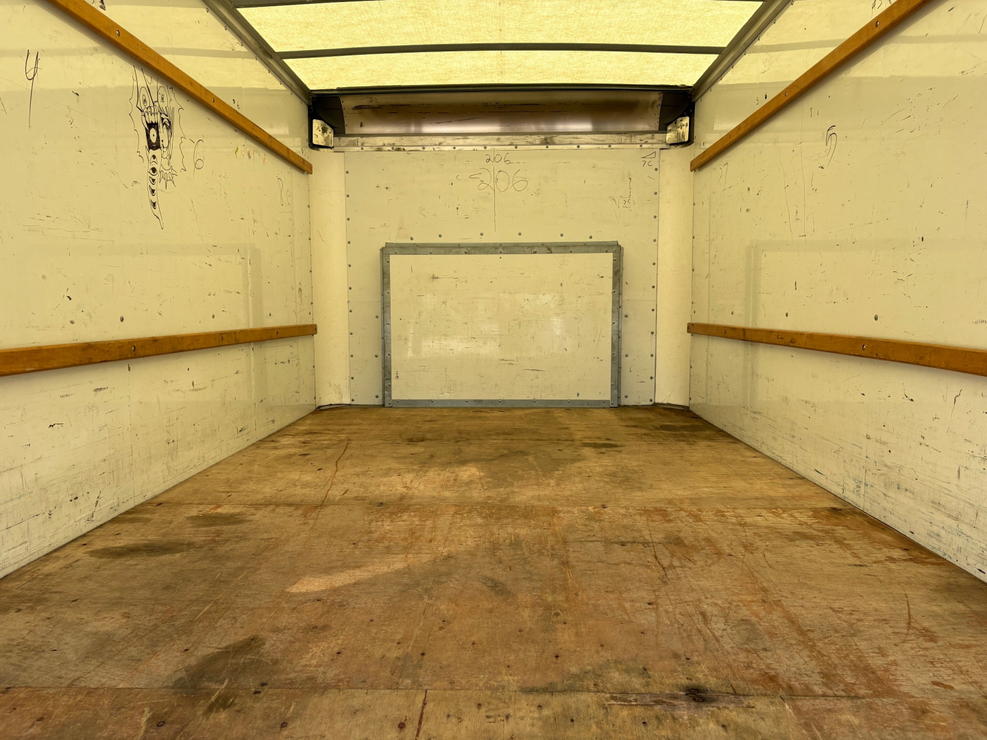 Truck cargo area inside a 2022 Ford E350 box truck showing empty wood-lined walls and a rear ramp door.