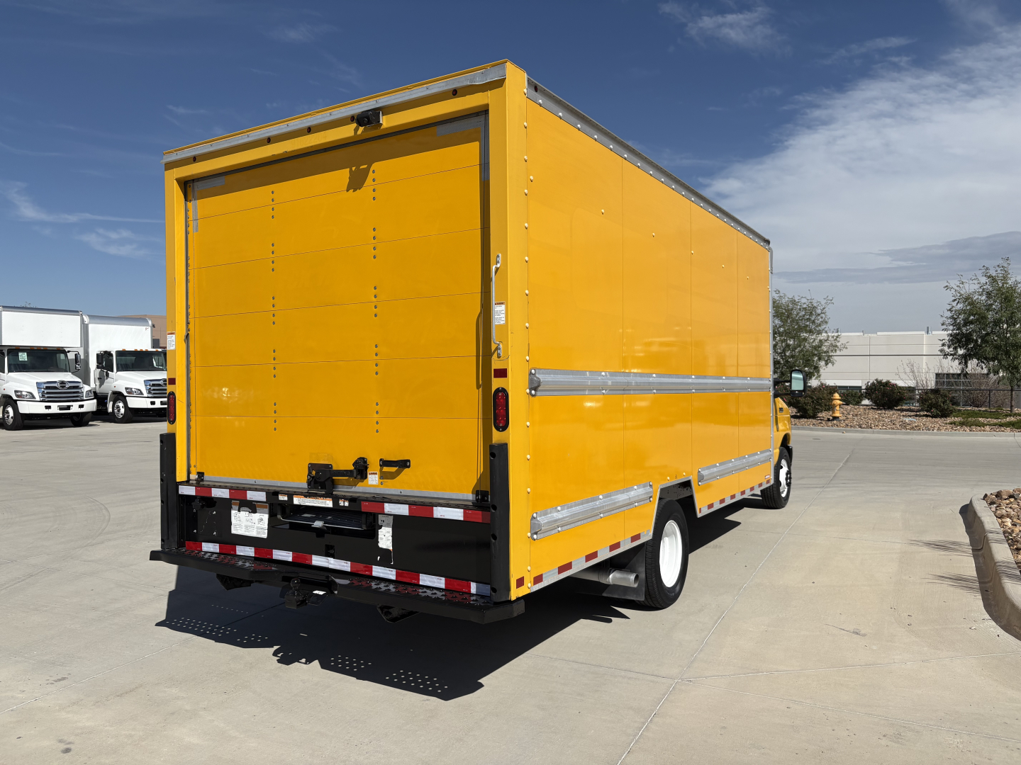 Yellow Ford E-350 cargo box truck rear-side view with back doors, stock stickers, and reflective strips.