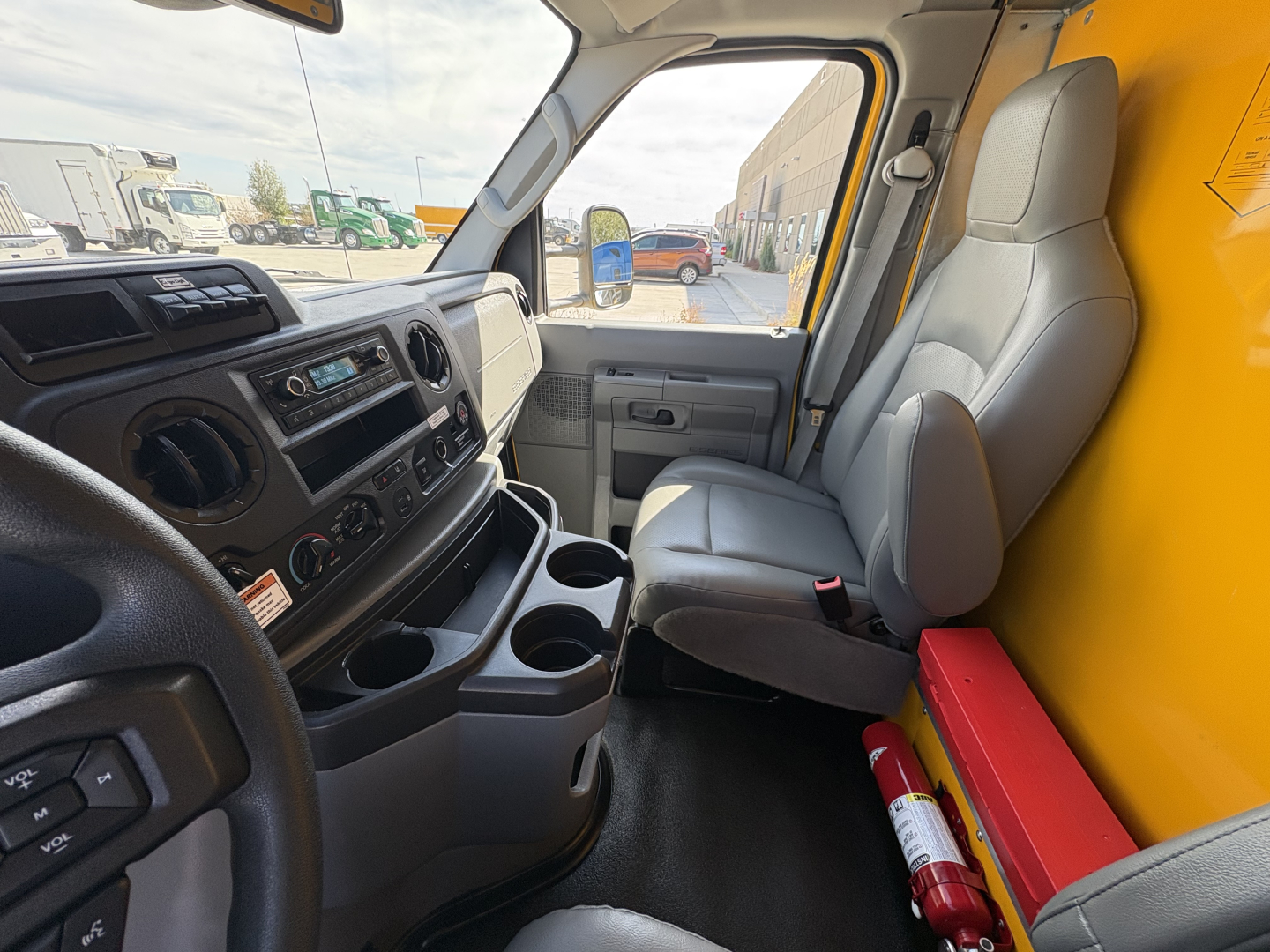 Ford E-350 interior driver side view showing dashboard with controls, steering wheel, center console, cup holders, passenger seat, and yellow partition behind seat.
