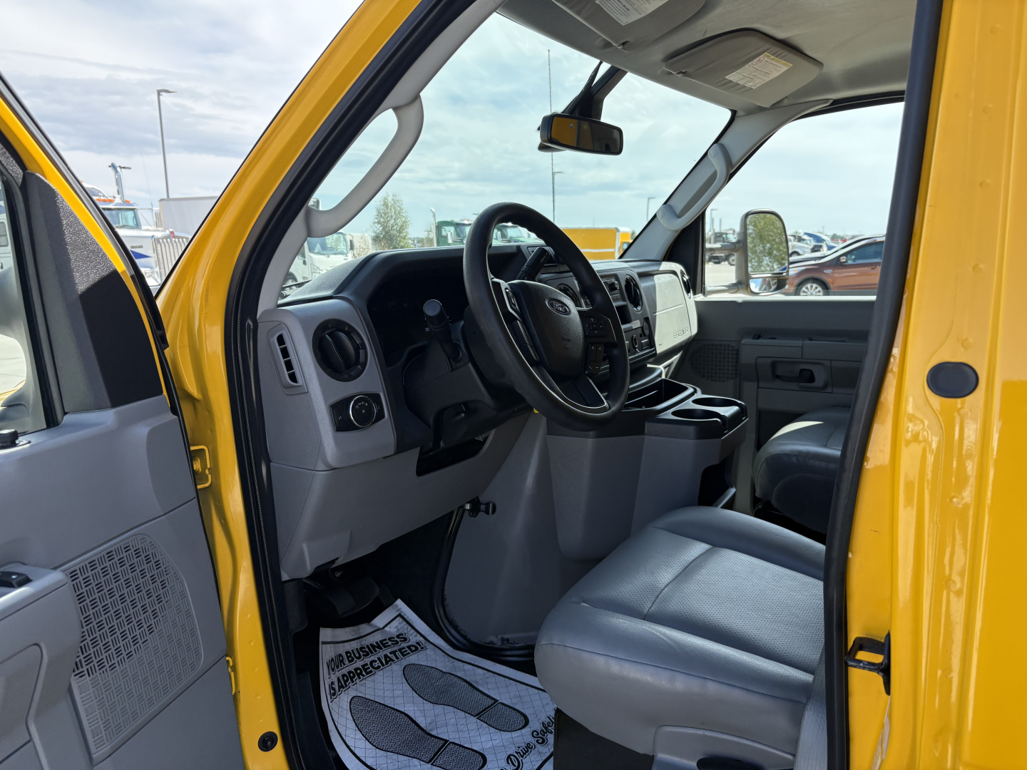 Ford E-Series cargo van interior showing steering wheel, dashboard, and front seats in gray; yellow exterior door frame visible.