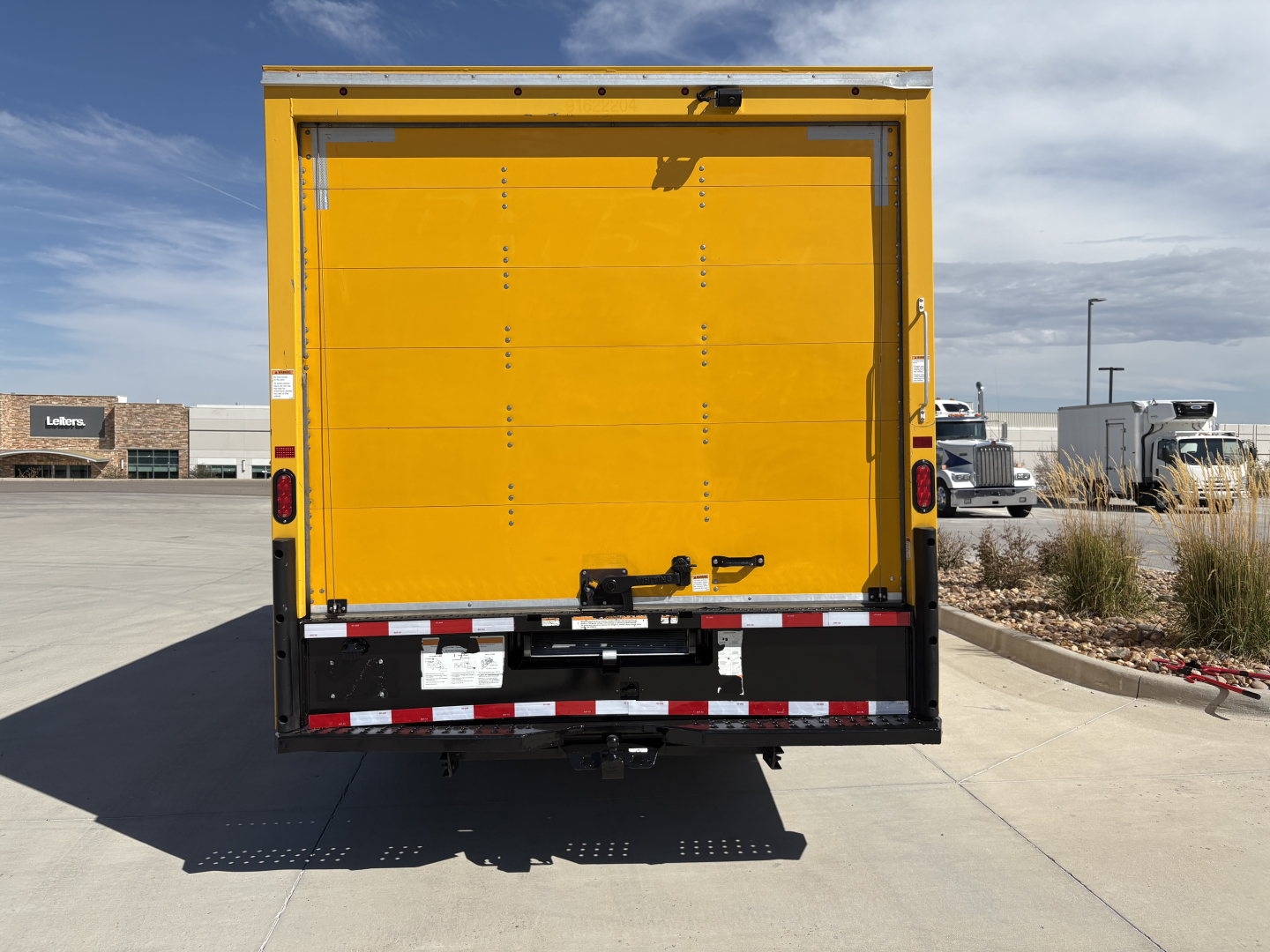 Truck rear view of a yellow Ford E350 cargo body with closed tailgate and rear lights.