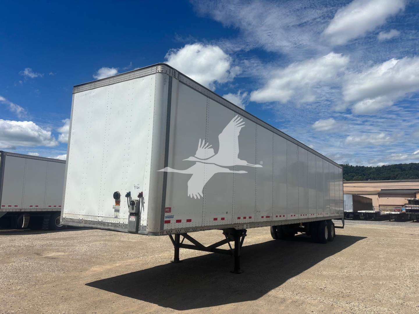 Trailer with a white body and a large hawk logo on the side showing a lift door and undercarriage from a side angle.