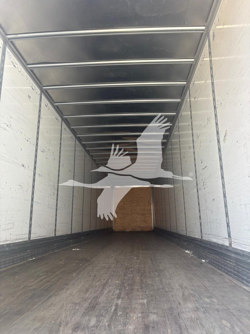 Trailer interior showing empty cargo space with wood bulkhead at far end and metal side rails.