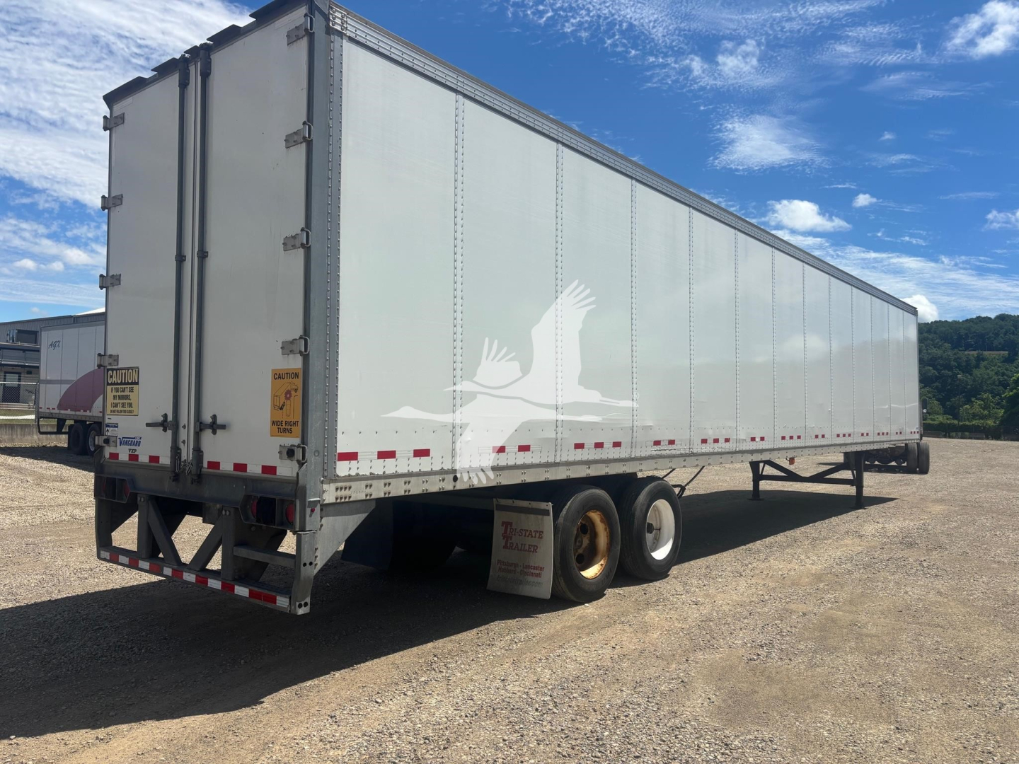 Trailer side view showing a 2017 Vanguard VXP box trailer with dual rear doors, tandem axles, white exterior and reflective tape.