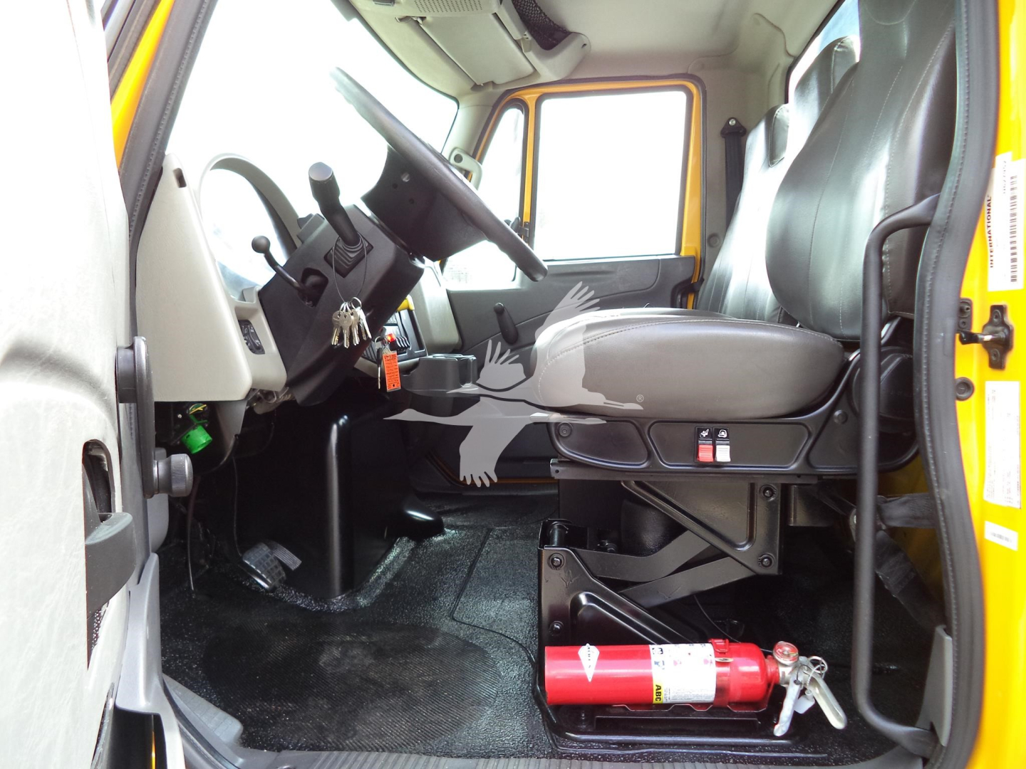 Truck cab interior of a 2019 International 4300 rollback showing driver's seat and dashboard with steering wheel and control levers.