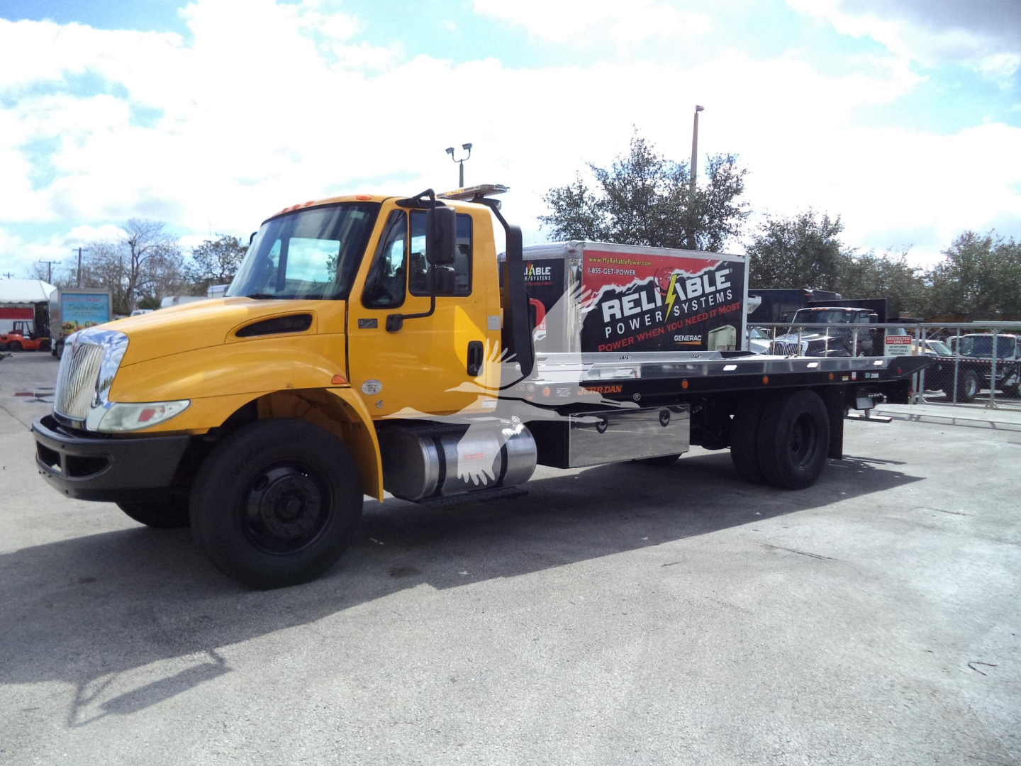 2019 International 4300 rollback tow truck with yellow cab and flatbed, side view showing ‘Reliable Power’ branding on the bed.