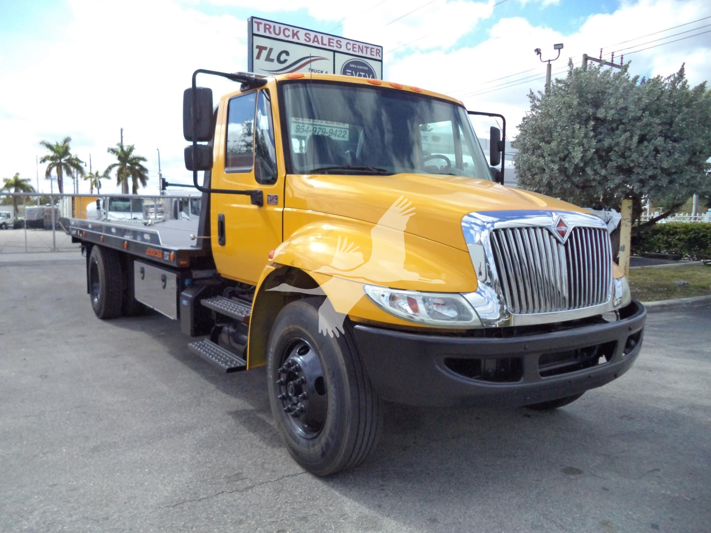2019 International 4300 rollback truck in yellow with flatbed, front view showing chrome grille and large side mirrors.