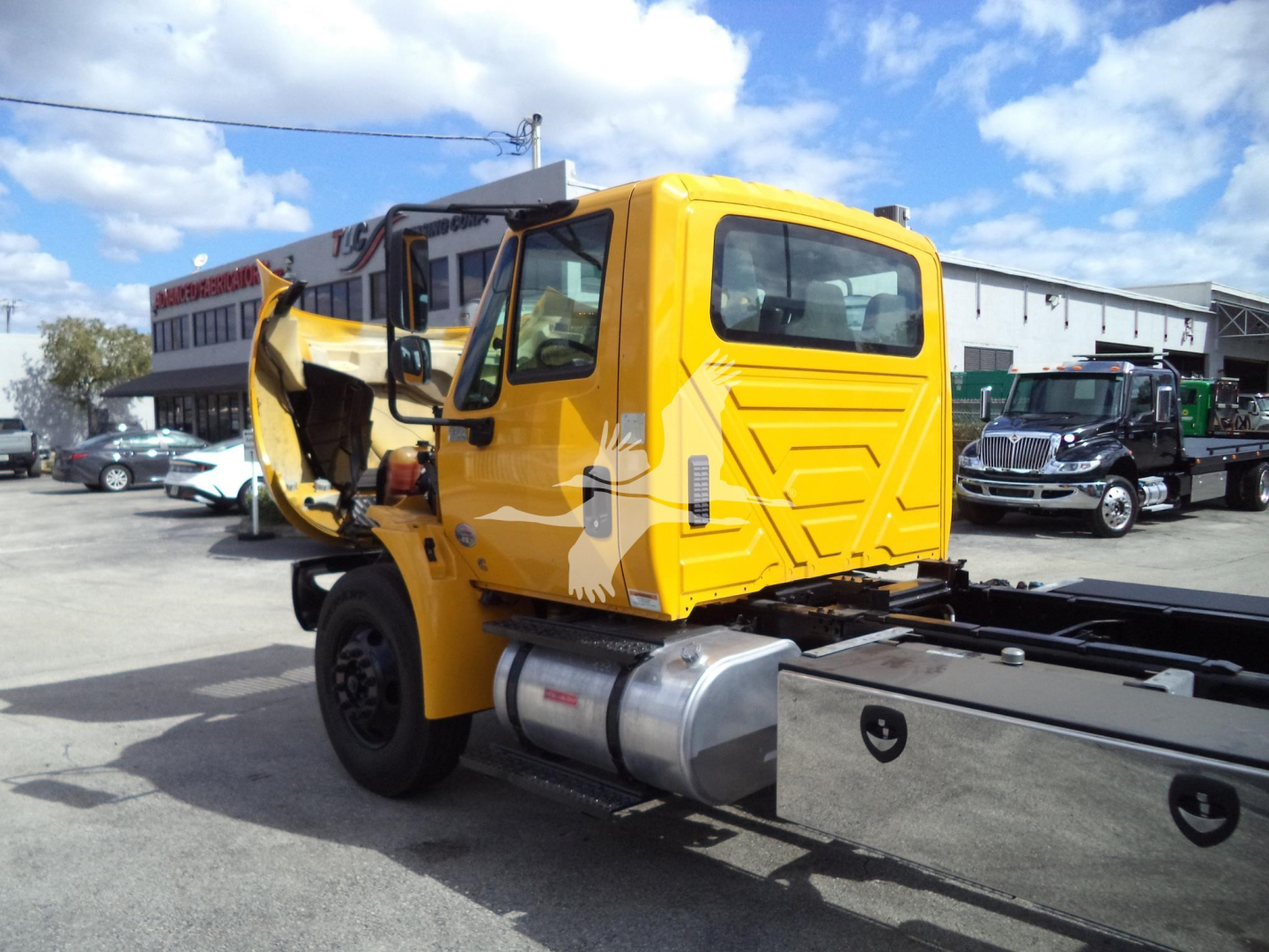 Yellow International 4300 rollback truck cab with open door and exposed engine area, side fuel tank, chassis rails, and rear cab window view.