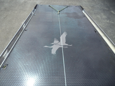 Flatbed or hydraulic rollback deck with diamond plate pattern, rope tied at front; silhouette of a bird logo painted on deck.