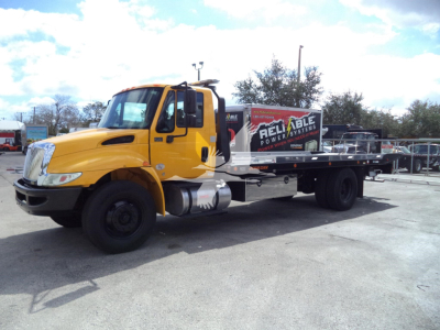 2019 International 4300 rollback tow truck with yellow cab and flatbed, side view showing ‘Reliable Power’ branding on the bed.